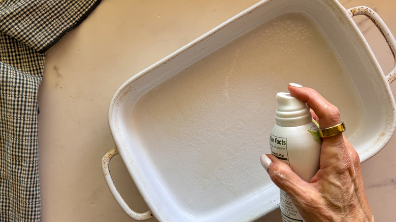 hand spraying baking dish with cooking spray