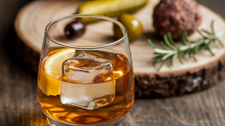 A close-up shot of a glass of whiskey in front of a log platter with ingredients placed on top