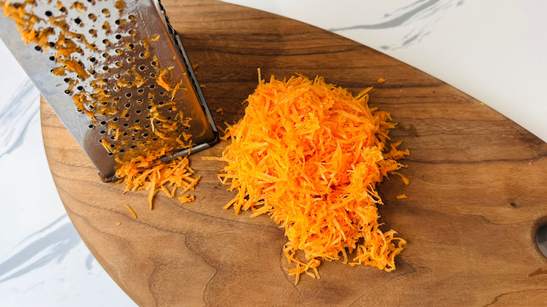 Box grater and grated carrot on wooden board