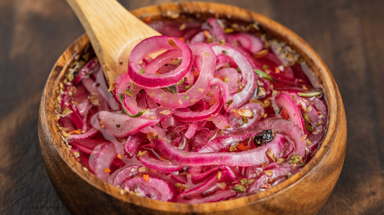 Pickled red onions in a wooden bowl with a wooden spoon scooping them up