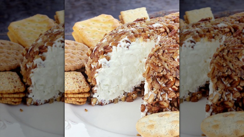 cheese ball sitting on a white plate with crackers and pretzels in the background.