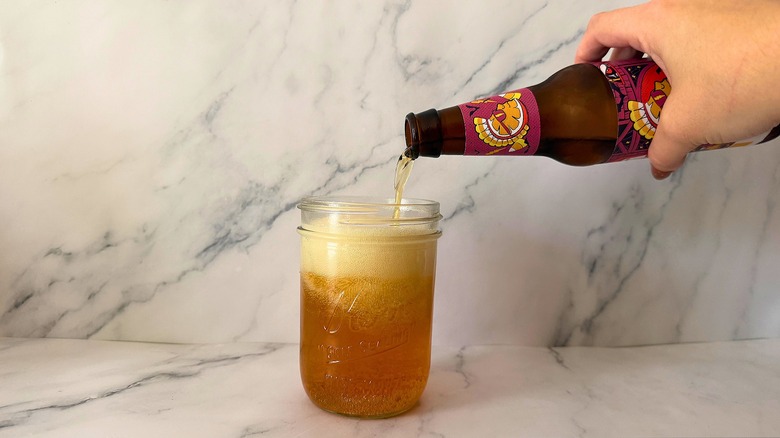 Hand pouring bottle of Shock Top Candy Corn Wheat Ale into mason jar glass on marble surface