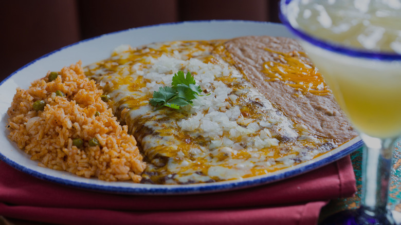 Plate of cheesy enchiladas, spicy rice, and refried beans next to cocktail served at Tex-Mex restaurant Candente