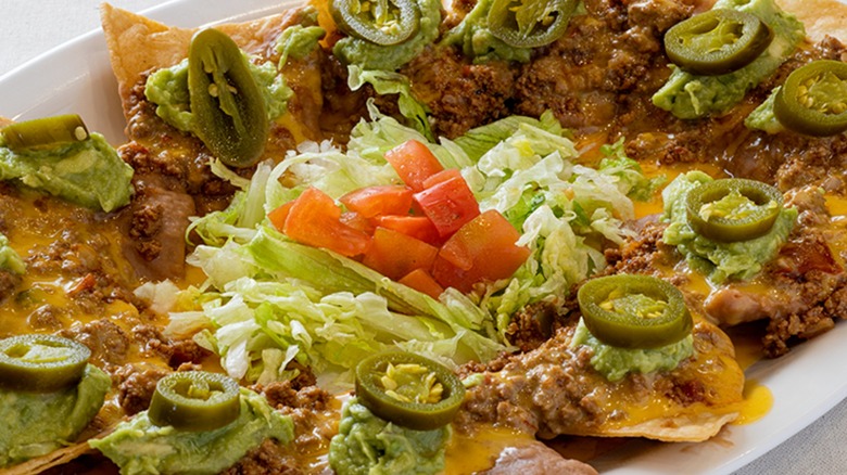 Close up of plate of nachos with shredded lettuce, diced tomato, and sliced jalapeños served at Los Tios, Houston
