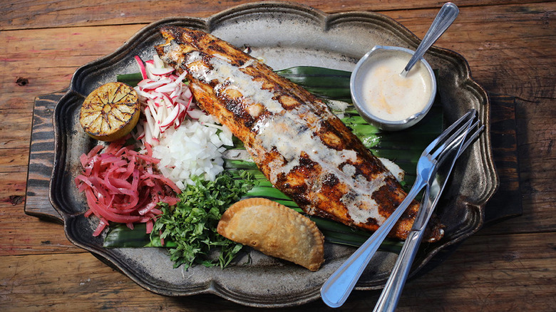 Plate of grilled fish with creamy sauce, an empanada, and crunchy vegetables at Goode Co. Kitchen & Cantina