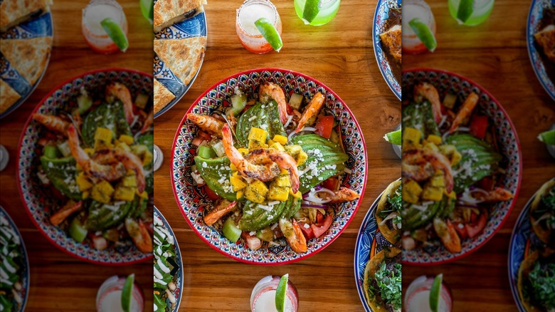 Colorful bowl of shrimp and avocado salad on table with cocktails at Cenas Kitchen