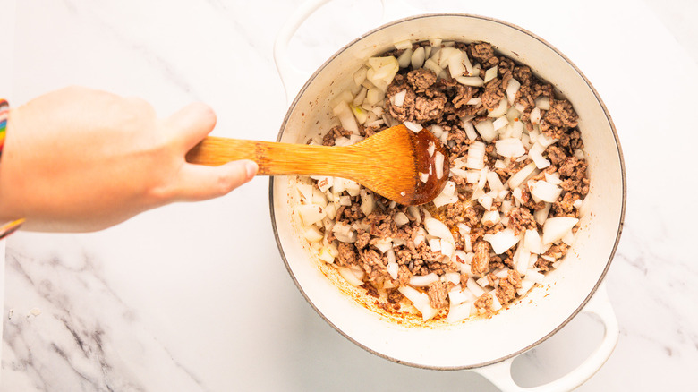 Adding onion to meat sauce in pot
