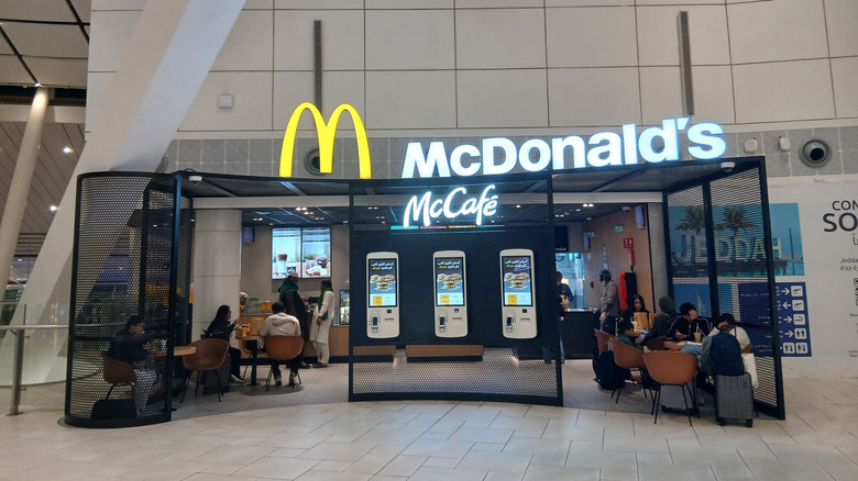 Diners are situated at tables inside an airport sectioned off underneath signs that read "McDonald's" and "McCafe".