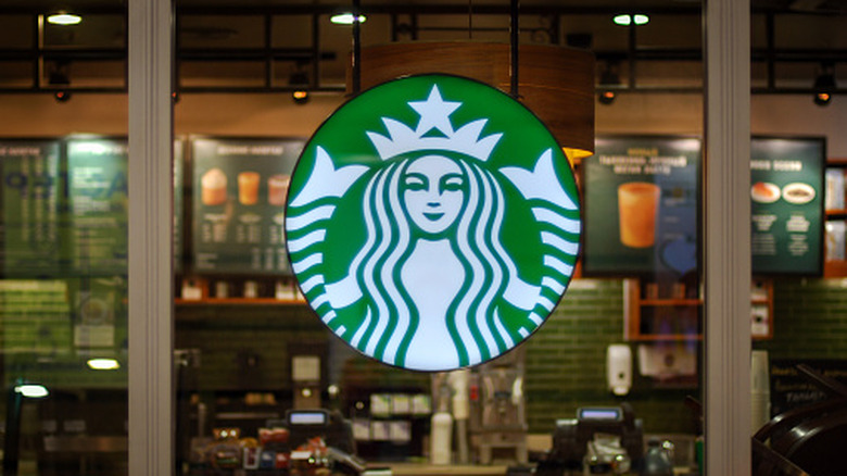 The Starbucks logo (a Mermaid against a green, circular background) appears in the forefront of the Starbucks store in the background.