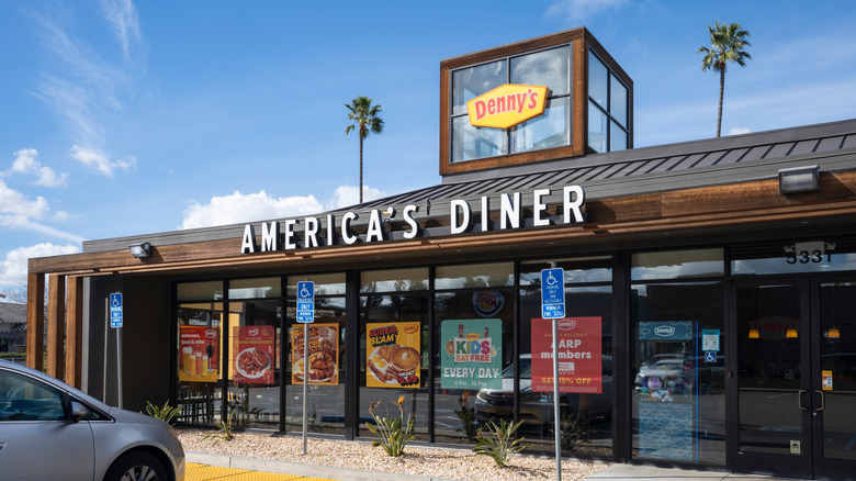 A Denny's storefront is pictured with a sign that reads, "America's Diner" above several marketing posters in the store's windows.