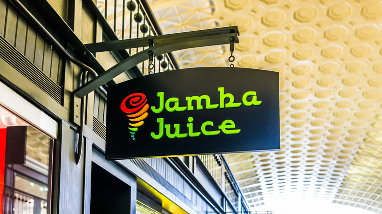 The exterior of a Jamba Juice is pictured, with the store name on a black sign hanging against wood paneling.