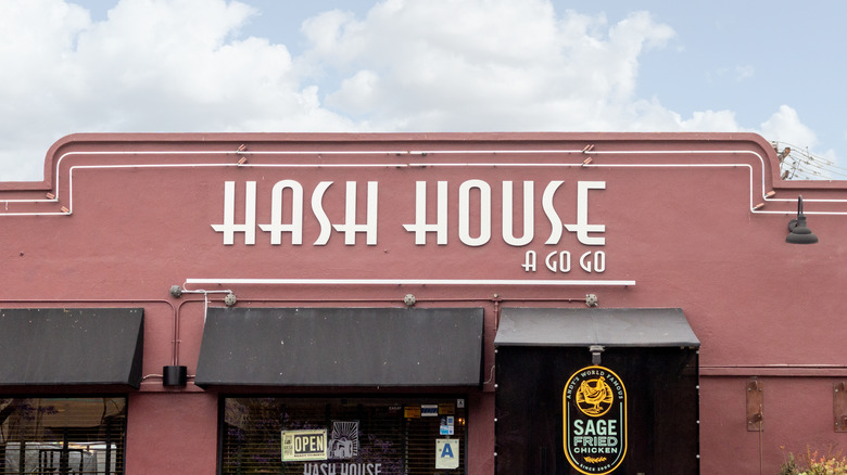 The exterior of a Hash House A Go Go restaurant is pictured against a cloudy, blue sky.