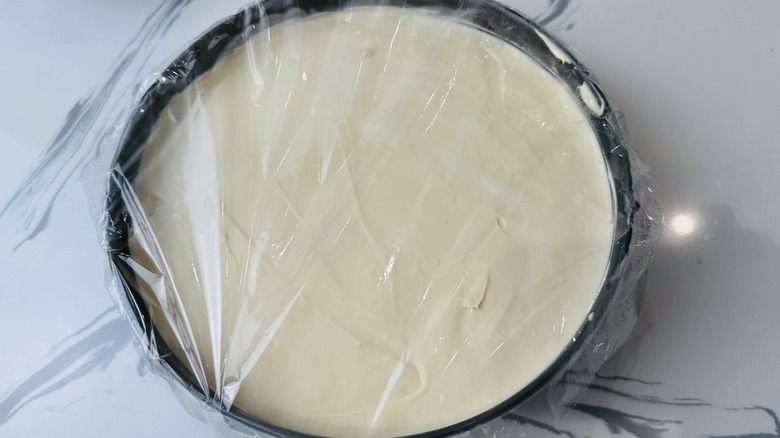Cheesecake in pan covered with plastic wrap