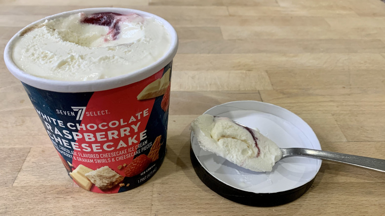 An open pint of 7-Select White Chocolate Raspberry Cheesecake ice cream, with one spoonful taken out.