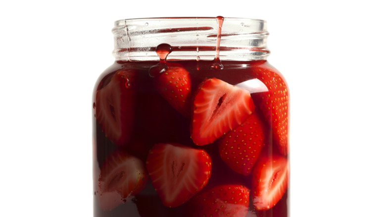 Glass with strawberry syrup on white background