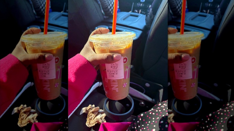 Hand holding Dunkin' drink in car