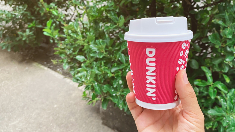 Hand holding a small Dunkin' hot drink outside