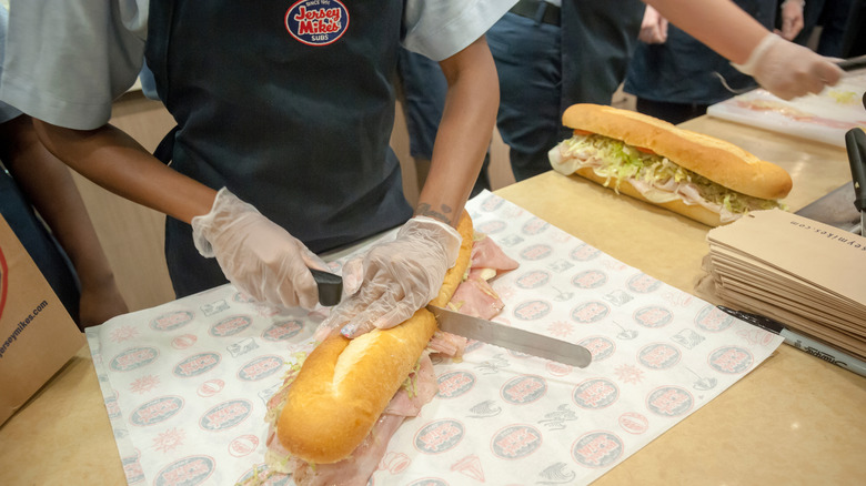 Employee slicing a submarine sandwich made Mikes Way