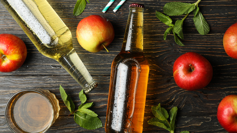 Bottles and a glass of hard apple cider and apples on a table