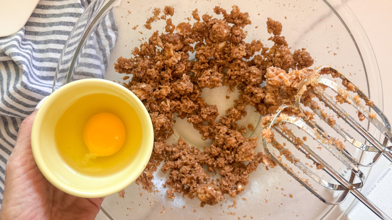 hand adding egg to bowl