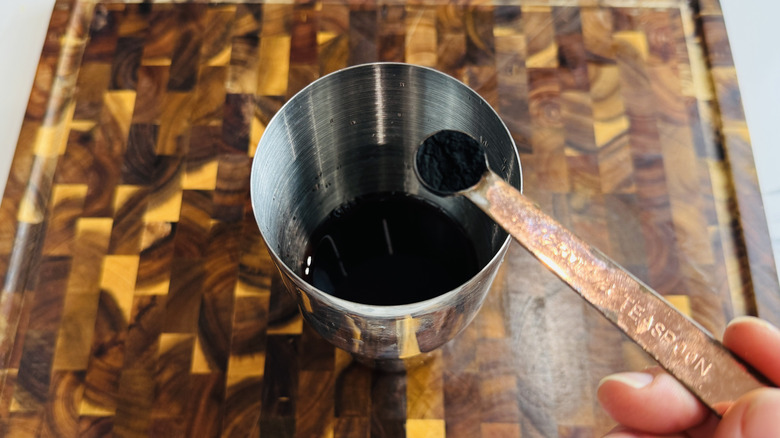 Activated charcoal powder in measuring spoon above cocktail shaker