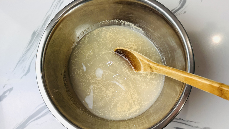 Water and yeast in bowl with wooden spoon