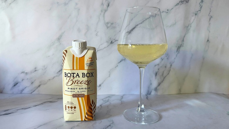 Mini Bota Box Breeze Pinot Grigio next to wine in glass on marble surface