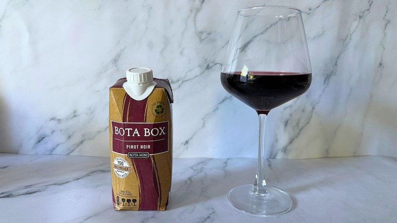 Mini Bota Box Pinot Noir next to wine in glass on marble surface