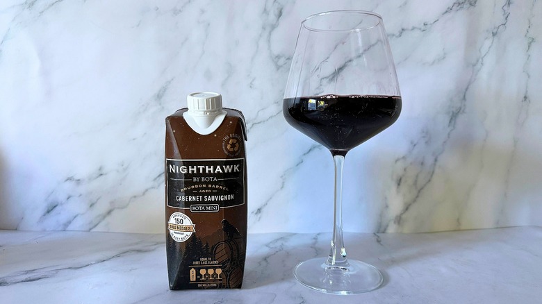 Mini Bota Box Nighthawk Cabernet Sauvignon next to wine in glass on marble surface