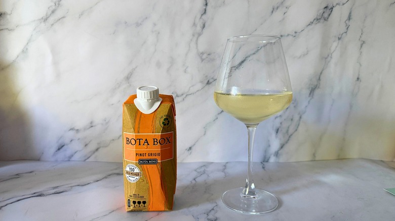 Mini Bota Box Pinot Grigio next to wine in glass on marble surface