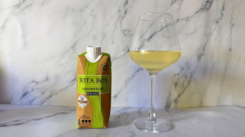 Mini Bota Box Sauvignon Blanc next to wine in glass on marble surface