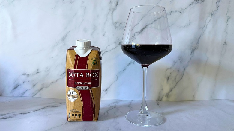 Mini Bota Box Redvolution next to wine in glass on marble surface