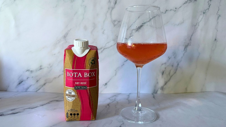 Mini Bota Box Dry Rosé next to wine in glass on marble surface