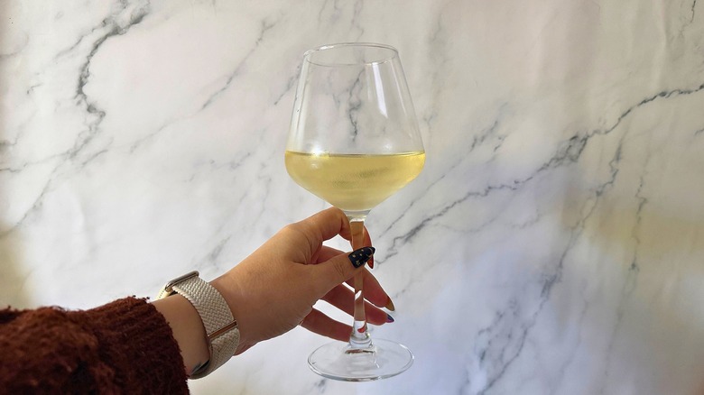 Hand holding glass of white wine against marble background