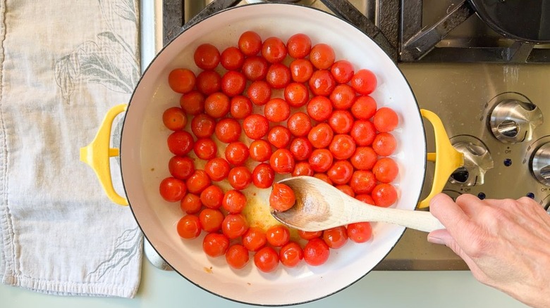 Blistered cherry tomatoes in Dutch oven on stovetop with wooden spoon