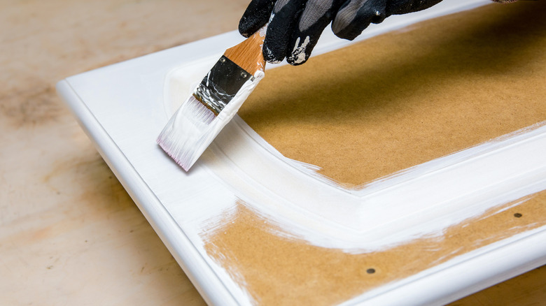 Hand painting with a paintbrush with white paint on wood cabinet.