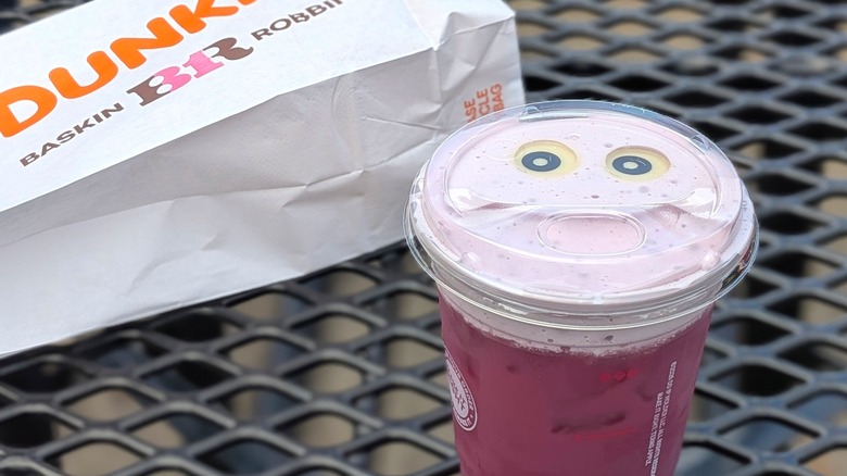 A close-up of the Berry Battie Daydream Refresher next to a white Dunkin' branded bag on a picnic table