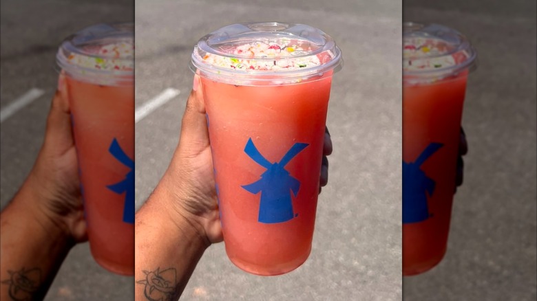 Hand holding Dutch Bros Stardust red fruit flavored drink with candy topping