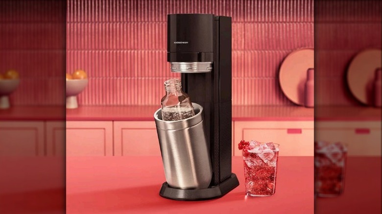 A manual SodaStream DUO sparkling water maker on a red countertop with a red background