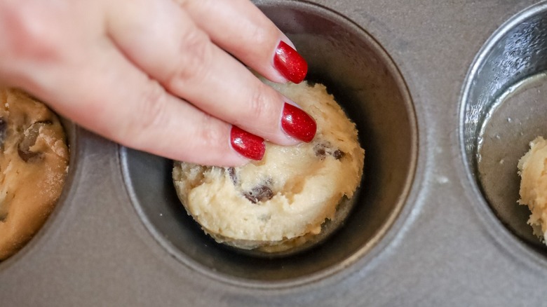 Hand pressing cookie dough into muffin tin well