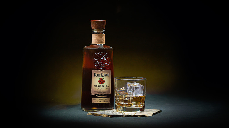 A stylized product shot of a bottle of Four Roses Single Barrel next to a filled glass on a piece of slate