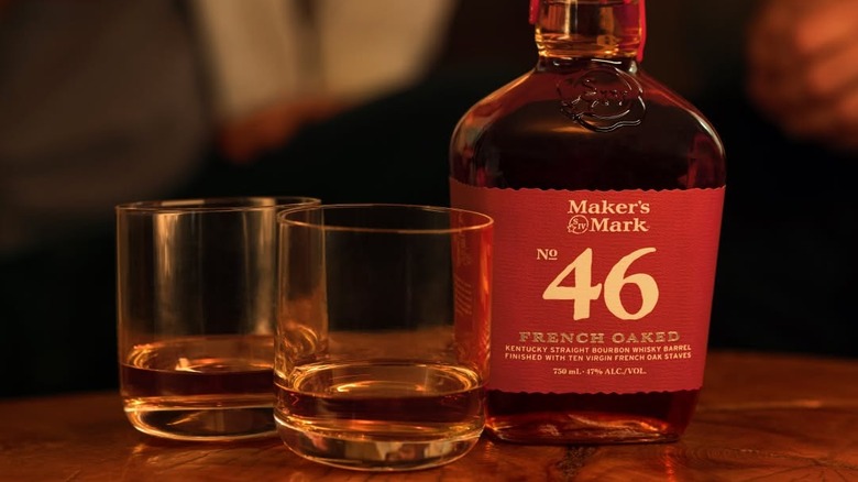 A bottle of Maker's Mark 46 placed on a table next to two filled glasses