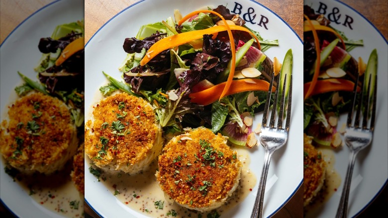 Two crab cakes on plate with sauce and greens
