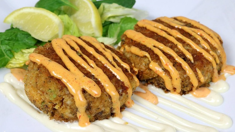 Two crab cakes with sauce, lemons, and lettuce