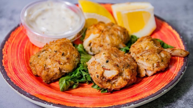 Four crab cakes with lemon and tartar on orange plate