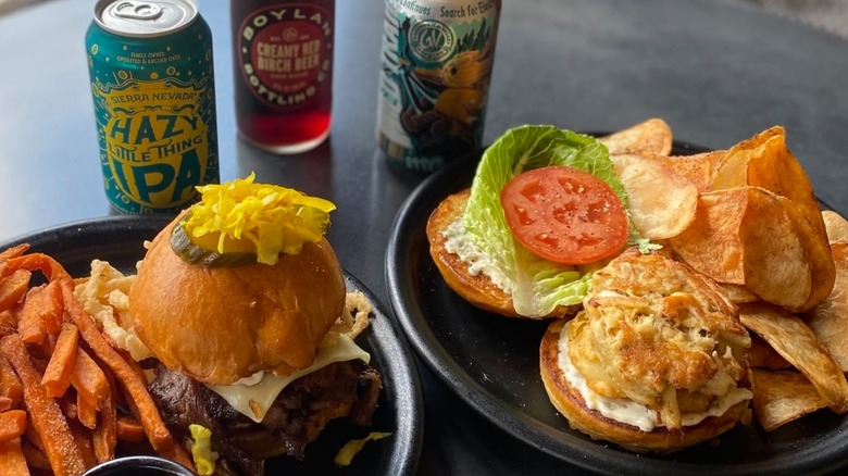 Crab cake sandwich with chips and burger alongside beer and soda