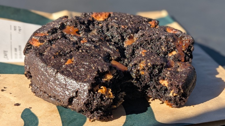 A close-up of a Venti Black Night Cookie with a bite taken out on a Starbucks paper bag