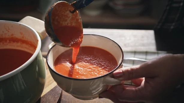 A person serving a bowl of tomato soup